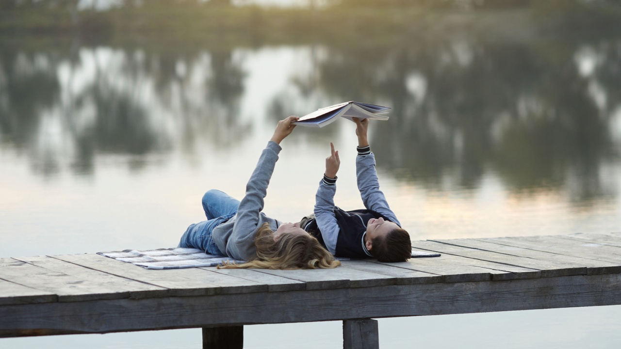 two kids lie on a dock reading a book together,