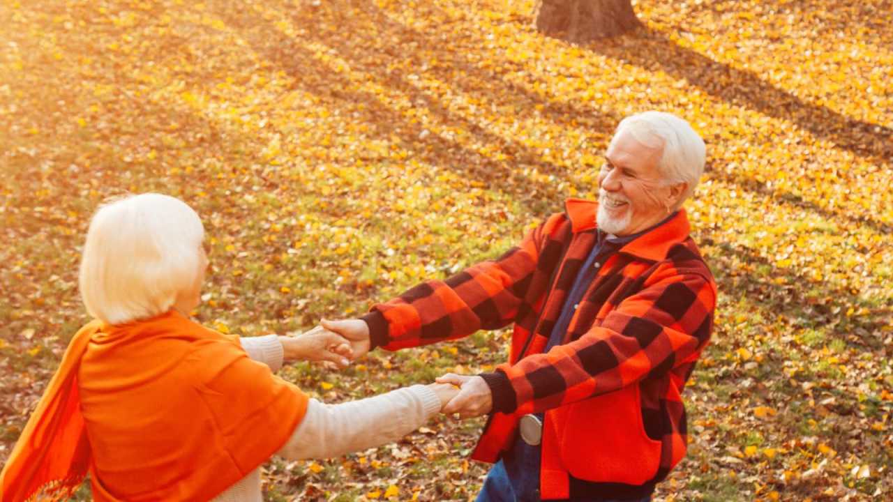 Elderly couple holding hands outdoors dancing and Smiling.