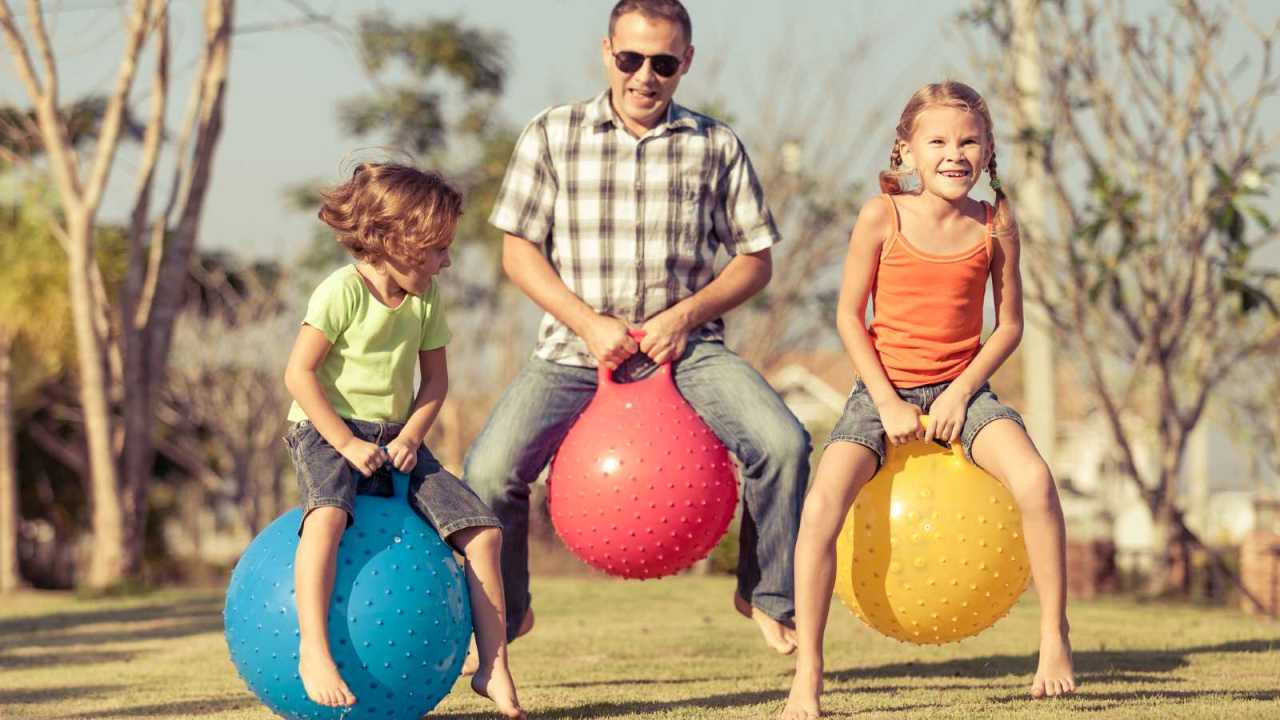 Happy Dad and children playing on lawn on hopping balls.