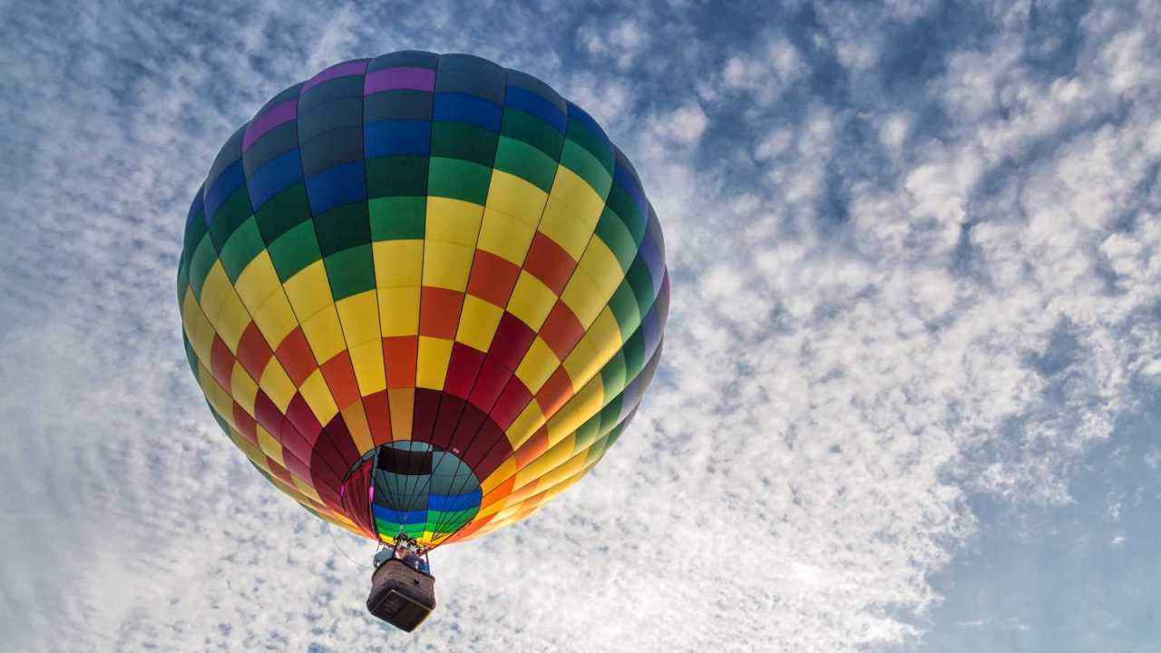 Rainbow hot air balloon in the sky with clouds.