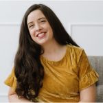 Amelia Bowler is wearing a yello shirt. She has long brown hair and smiles in a friendly way at the camera.