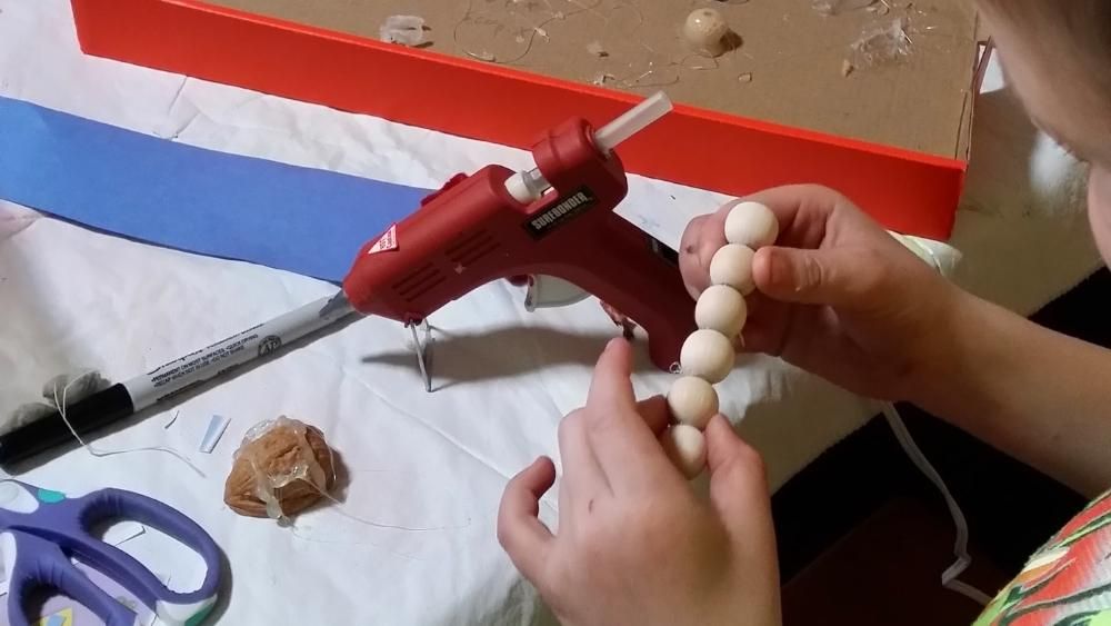 A child sits by a glue gun gluing wooden beads together