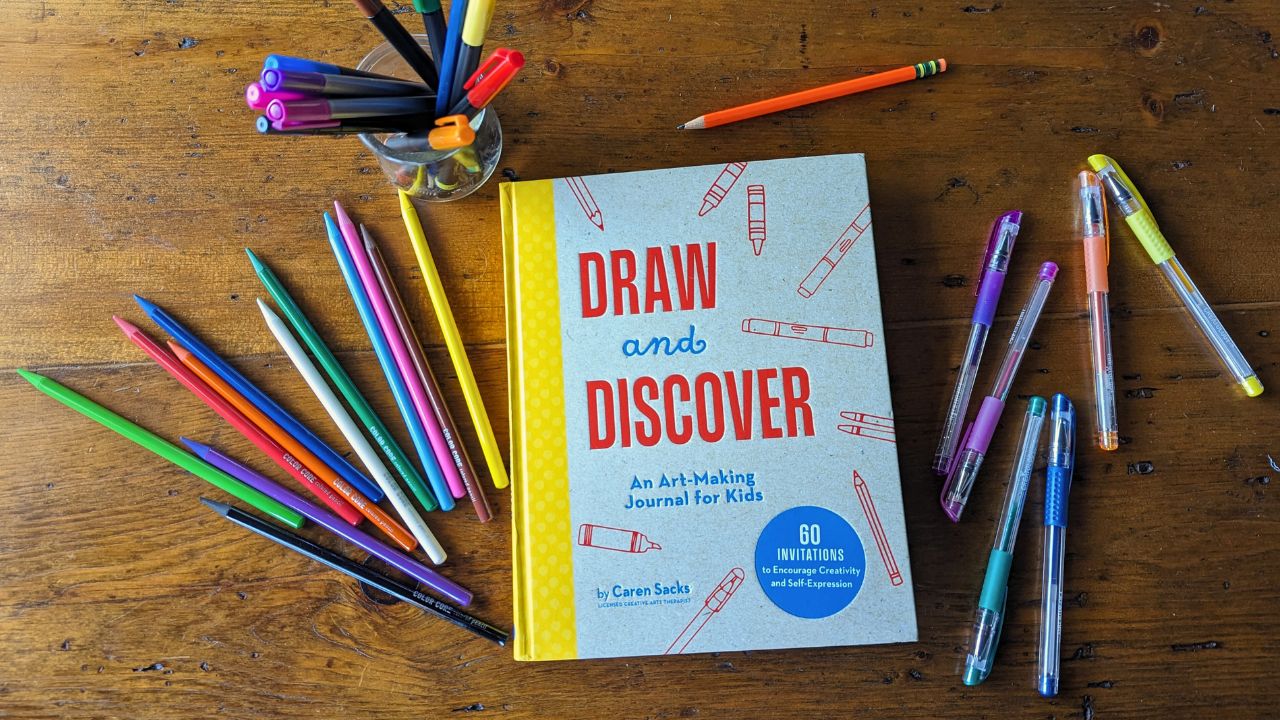 Overhead view of Draw and Discover Art Journal for Kids book surrounded by art supplies.