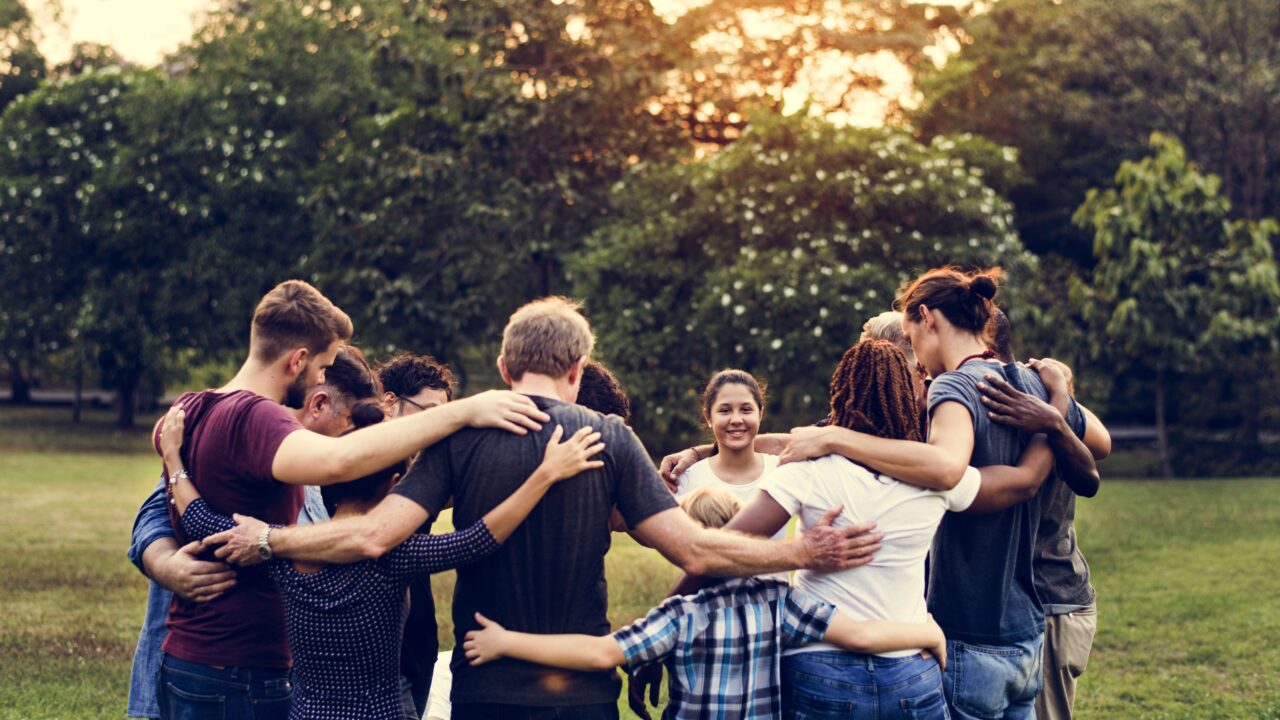 Group of people outdoors in park link arms supporting one another.